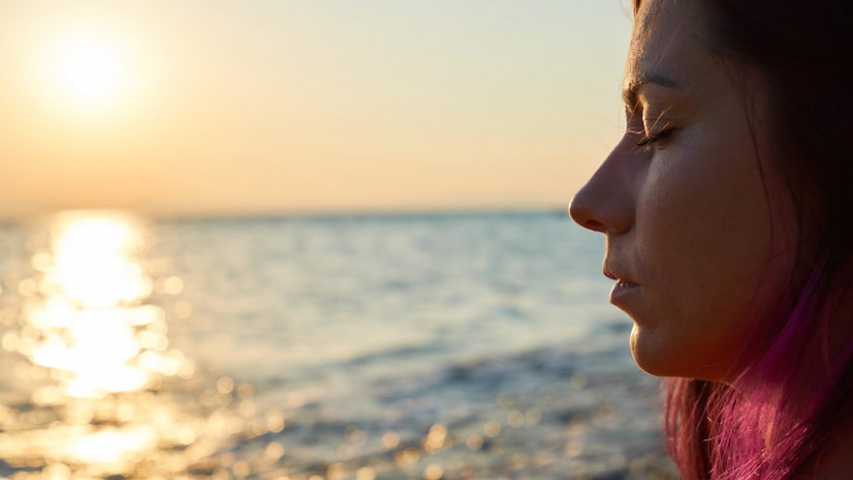 Young woman with eyes closed looking out onto the ocean