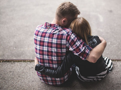 male in a flannel shirt hugging a girl wearing a leather jacket. image for supporting someone with cancer