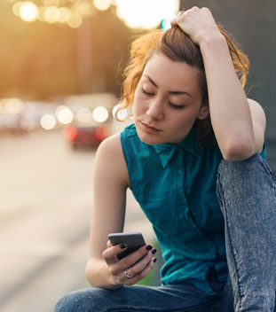 young female with her hand scrunching her hair and looking through her phone for help for cancer patients