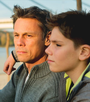 young son with his arm over his dad wearing a grey jumper. image for family support for cancer patients & family cancer