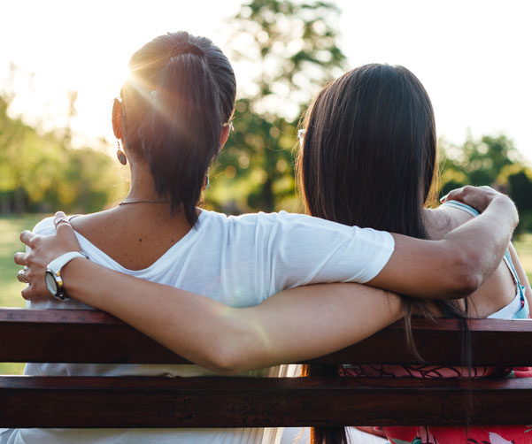 Two young people impacted by cancer hugging on a chair - Canteen