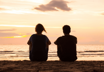 Mum and son sit on beach looking into the sunset