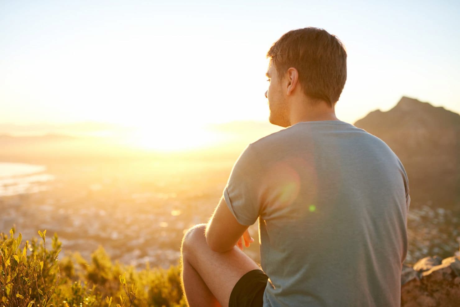 young person sitting on a mountain and looking into the sunset
