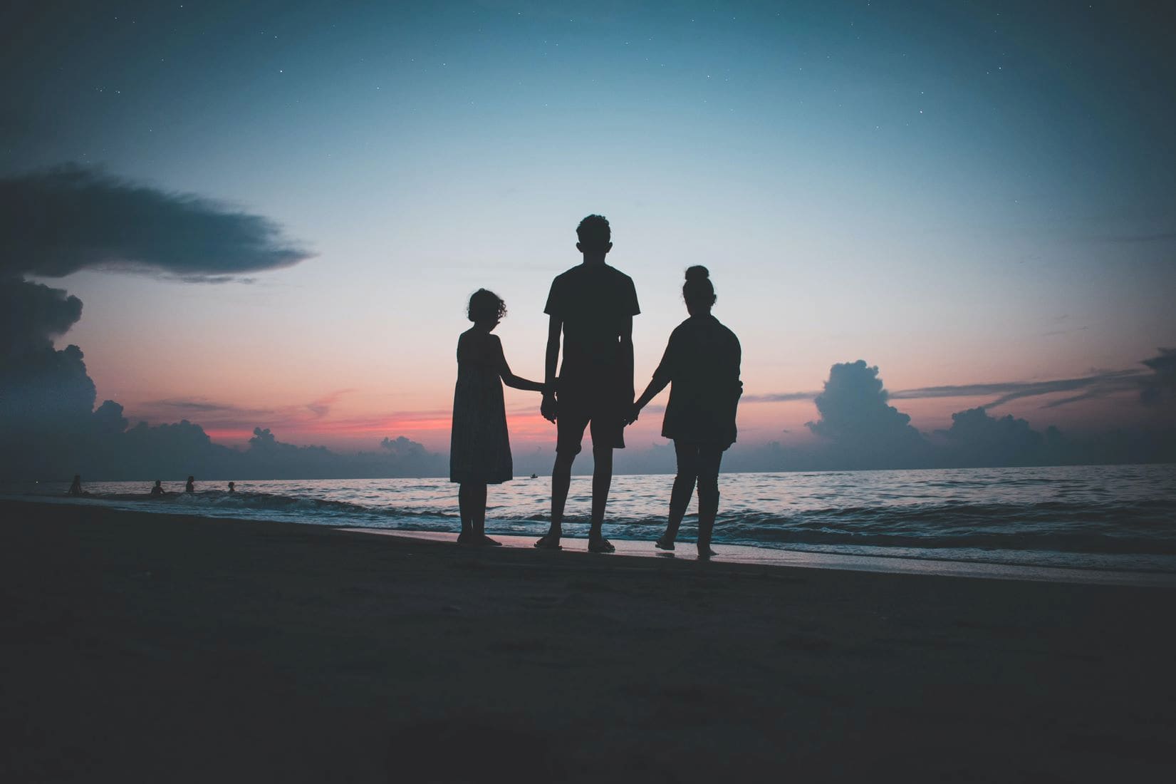 three siblings impacted by cancer standing on the beach