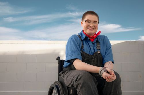 a young person in a wheelchair smiling at the camera wearing a canteen bandanna