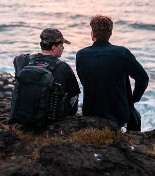 two males sitting on a rock by the ocean having a conversation. image for youth cancer services and young adult cancer