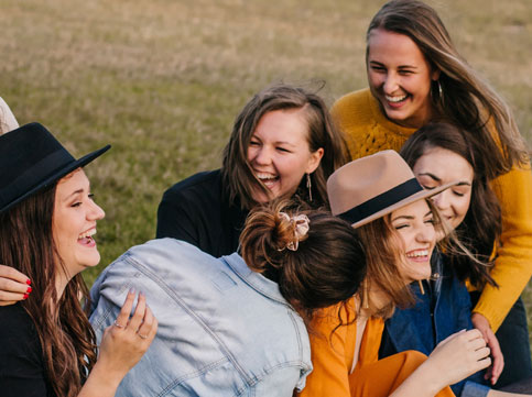 six female friends laughing and hugging each other at a park - image for youth cancer services and young adult cancer