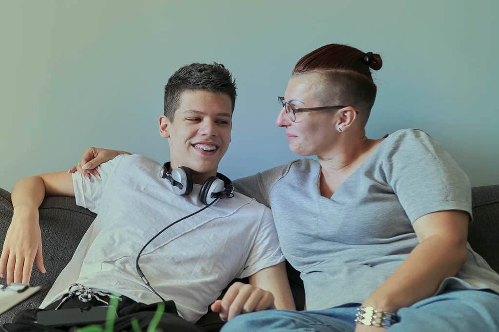 a child and parent who have been impacted by cancer in the family are sitting on the couch, hugging and talking with each other