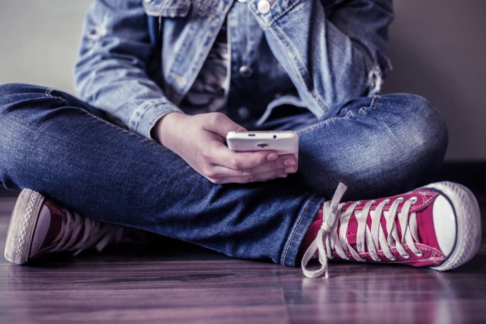 young person crossing their legs and sitting on the floor while using their phone