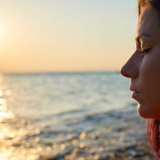 Young woman with eyes closed looking out onto the ocean