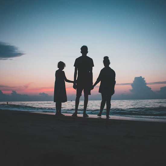 Three siblings hold hands on a beach