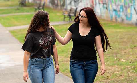 Two Canteen young people walking in a park together, one with her arm round the other showing support