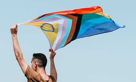 A young person holding up an LGBTQI+ flag