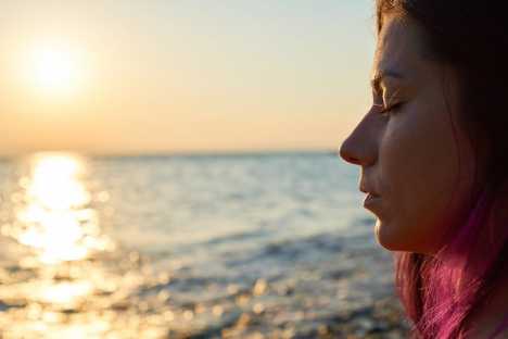 Young woman with eyes closed looking out onto the ocean