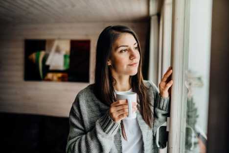 Young woman holding cup looking out window