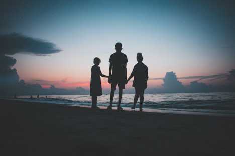 Three siblings hold hands on a beach