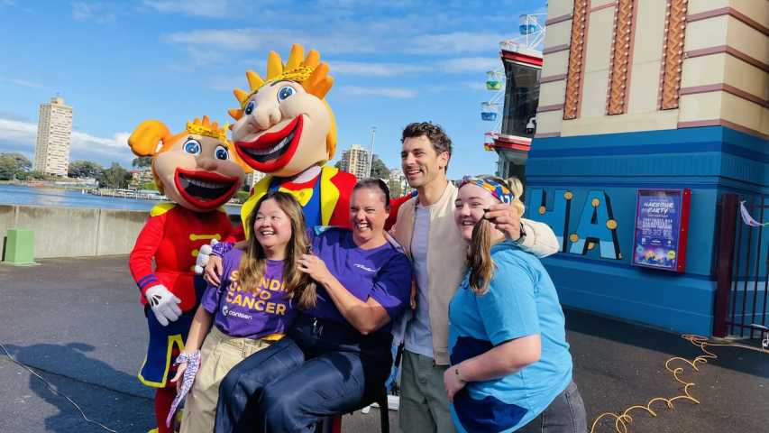 Four young adults in front of Luna Park with the Luna Park characters after one person shaved their head for Canteen's Bandanna Day