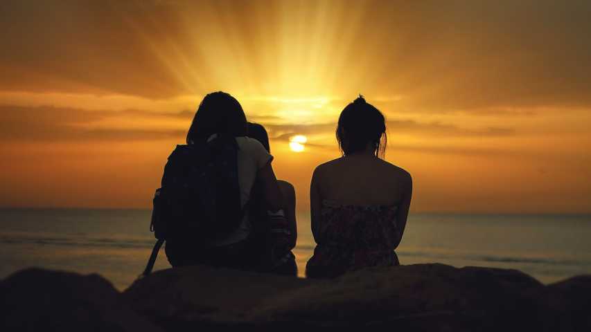 three young people sitting and looking into the sunset