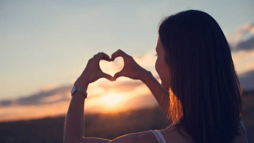 young person making a heart shape with her hands in front of the sky