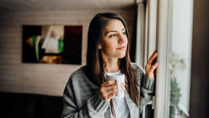 Young woman holding cup looking out window