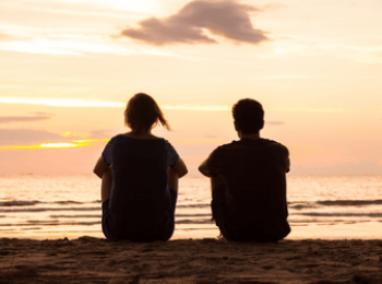 Mum and son sit on beach looking into the sunset