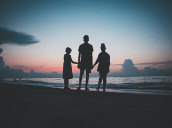 Three siblings hold hands on a beach