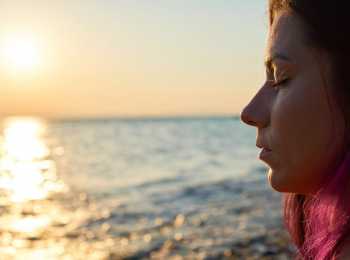 Young woman with eyes closed looking out onto the ocean