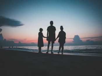 Three siblings hold hands on a beach